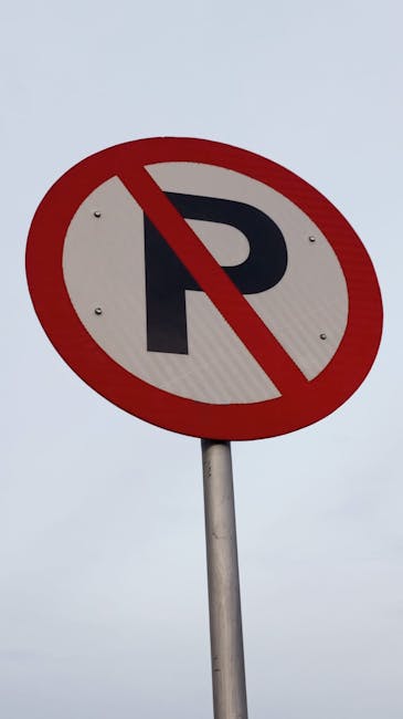 A street scene featuring a white speed limit sign indicating a maximum of 10 miles per hour, mounted on a yellow pole alongside a traffic light with red, yellow, and green signals. Below the speed limit sign, there is a white and red no parking sign with a red circle and slash over a capital 'P', accompanied by the words 'NO PARKING' and an arrow pointing left. The background shows part of a building with a cantilevered roof extending over the sidewalk and some cloudy sky. This setting reflects urban parking and traffic regulation signage, relevant to house removals and moving logistics in Pimlico, with the presence of signage managed by Man with Van Pimlico for relocation activities.