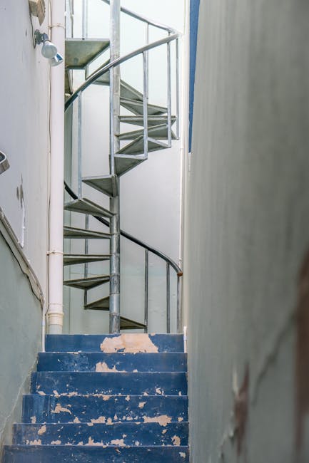 Image of a narrow wooden staircase inside a building, accessed through a small doorway with a wooden frame. The staircase has approximately six worn, dark-colored steps that are slightly uneven, leadi
